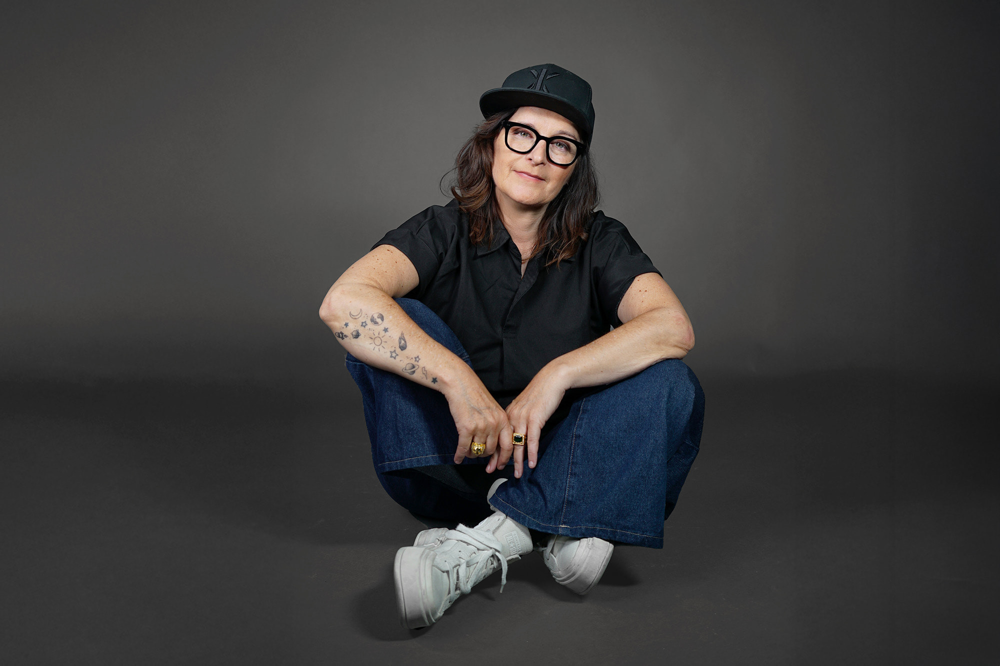 Bild von Anja Maria Welzel wie sie sitzend in die Kamera guckt. Sie trägt ein Cap und eine Brille.