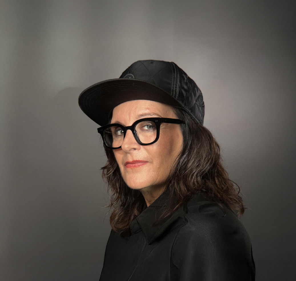 Bild von Anja Maria Welzel wie sie im Profil in die Kamera guckt. Sie trägt ein Cap und eine Brille.